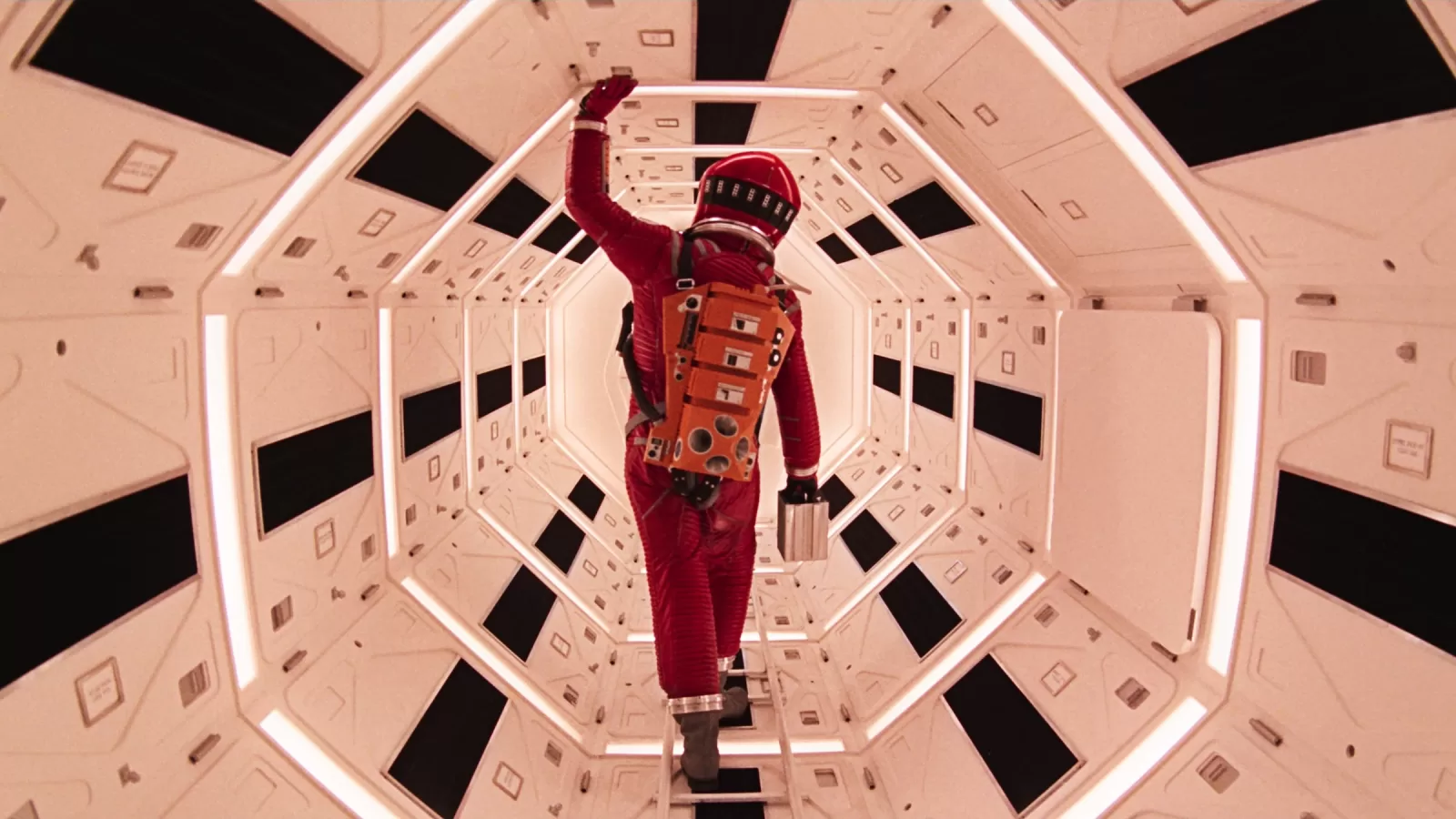 Un astronauta con traje espacial rojo camina por un pasillo blanco y hexagonal de una nave espacial