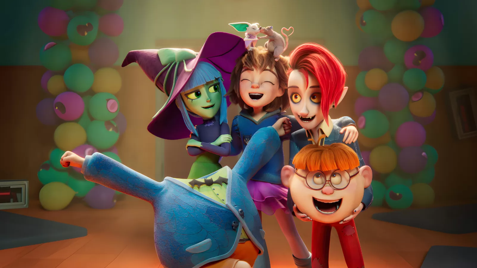 Niña sonriente rodeada de una bruja verde, un vampiro pelirrojo y un niño de lentes en un salón con globos de colores