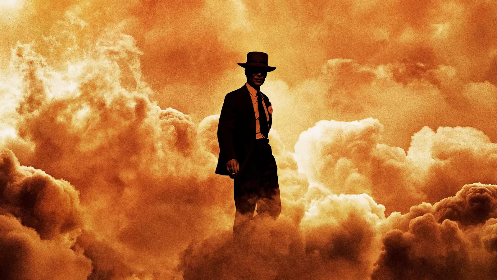 Un hombre con sombrero y abrigo, visto de espaldas, se recorta contra una enorme nube de fuego anaranjada