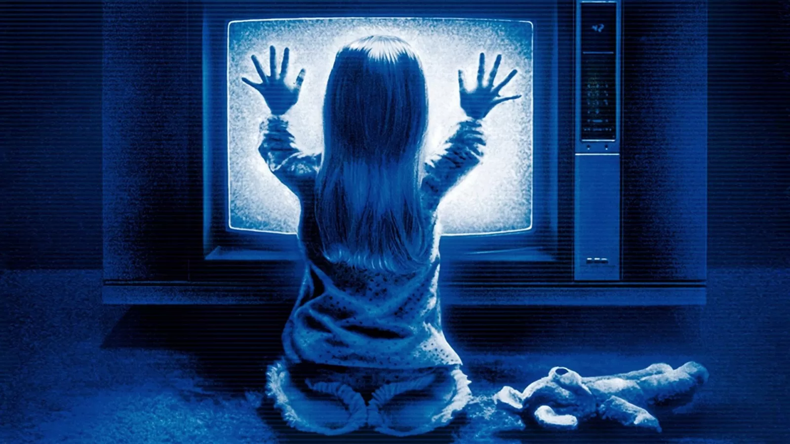 Una niña rubia en pijama, de espaldas y arrodillada, apoya las manos en la pantalla de un televisor encendido con estática